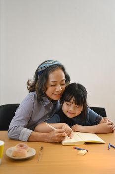 Smiling middle aged grandma and little preschooler granddaughter drawing together at home.