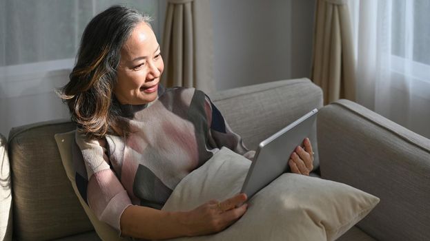 Happy mature woman reading news online, checking social media on tablet. Elderly technology concept.