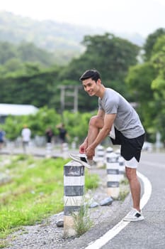 Young sportsman tying shoelaces before running, getting ready for jogging outdoors. Healthy lifestyle and wellness concept.