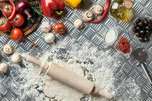 Ingredients and dough for making pizzas with an overhead view on freshly mixed mounds of pastry, a jar of olive oil and pot of tomato sauce, overhead view on metal background. Top view. Flat lay. Still life