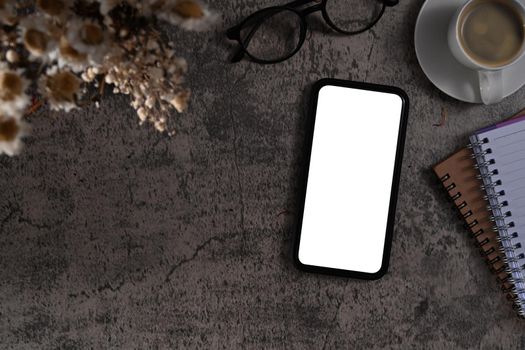 Top view mockup mobile phone with blank screen, eyeglasses an coffee cup on ark stone background.