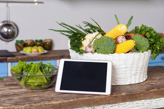 Tablet pc, fresh vegetables and cooked salad on wooden table in modern kitchen, concept of online cooking tips for healthy vegetarian low-calorie diet, food recipes, menu and blog, vegan nutrition