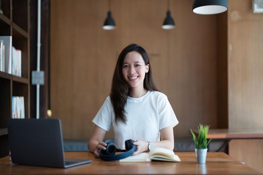 portrait smiling Asian young woman looking at camera, attractive female freelance online working from home with laptop. online learning education concept.