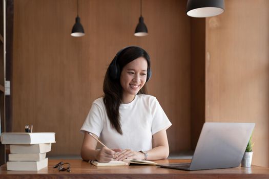 Happy asian woman sit at desk at home write study online on computer. Smiling young mixed race female work distant on laptop, take course on web. Education, learning concept