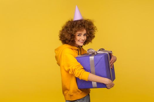 My precious. Portrait of happy pleased curly-haired woman embracing huge gift box and smiling to camera, satisfied with enormous birthday present. indoor studio shot isolated on yellow background