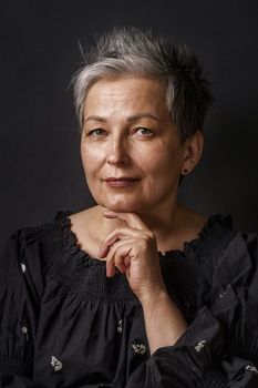 Close up gorgeous mature businesswoman with grey hair posing leaned chin on her hand isolated on black background. Graying elegant woman with short hair. Image of successful mature woman. Aged beauty.