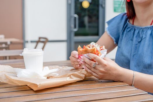 Summer vacation, street food eating. closeup of woman hands holding hamburger, woman eating fast food at street cafe