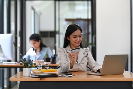 Happy young female office worker holding credit car and shopping online on laptop computer.