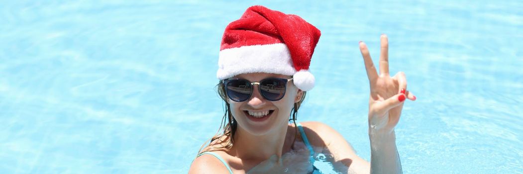 Young smiling woman in santa claus hat in pool. Winter Holidays tourism and recreation concept