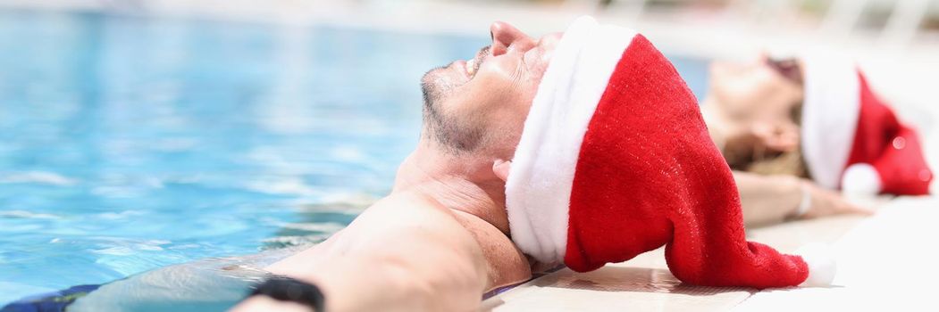 Young people in santa claus hats lie relaxed in pool. Tourism vacation for New Year holidays concept