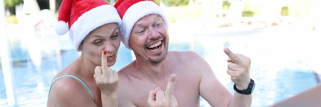 Man and woman in santa claus hats show fucking gesture into monitor. Remote work and rest in quarantine concept