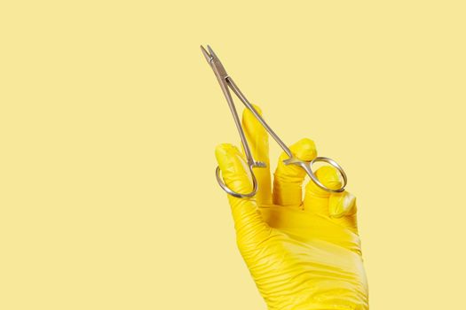 Woman's hand in a latex glove with stainless steel needle holder on yellow.