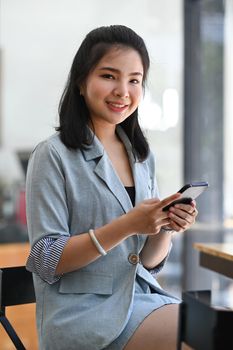 Portrait of beautiful young asian woman sitting in modern coffee shop and using mobile phone.