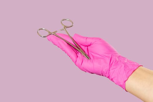 Woman's hand in a latex glove with stainless steel needle holder on pink.