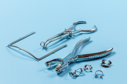 Dental hole punch, metal clamps, a metal frame and a rubber dam forceps on the blue background. Medical tools concept.