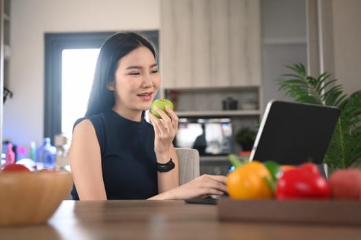 Healthy young woman eating apple and using digital tablet in the kitchen. Healthy lifestyle concept.