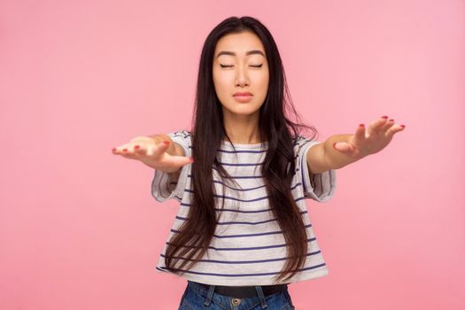 I can't see. Portrait of brunette girl in striped t-shirt standing with closed eyes and outstretched hands, trying to find obstacles while walking blind. indoor studio shot isolated on pink background