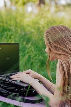 On the banner, a young girl works with a laptop in the fresh air in the park, sitting on the lawn. The concept of remote work. Work as a freelancer. The girl takes courses on a laptop and smiles