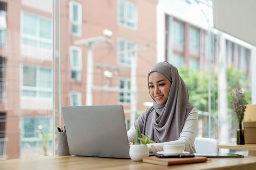 Young asian muslim business woman in smart casual wear discussing business and smiling while sitting in the creative coworking