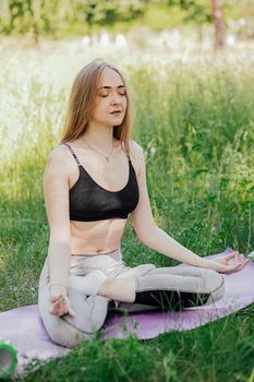 Yoga woman on green grass girl relaxes in the field. Yoga woman in green park girl doing gymnastics outdoors. Meditating woman in meditation in yoga pose practices outdoors