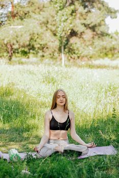 Yoga woman on green grass girl relaxes in the field. Yoga woman in green park girl doing gymnastics outdoors. Meditating woman in meditation in yoga pose practices outdoors