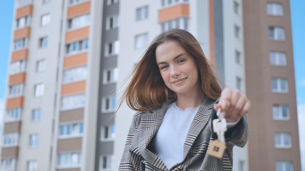 The girl shows the keys to the apartment against the backdrop of an apartment building