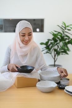 Beautiful Muslim woman online seller packing product in cardboard box for shipping to customers.
