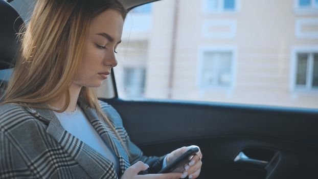 A young girl rides in the backseat of a car and watches her smartphone