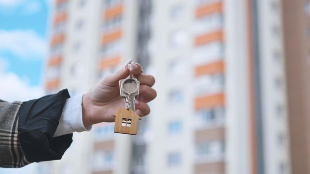 Girl holding keys to apartment against the backdrop of an apartment building