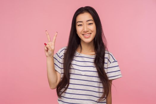 Concept of winning. Happy lucky joyful girl with long hair showing v sign, victory or peace hand gesture and smiling broadly, celebrating success. indoor studio shot isolated on pink background