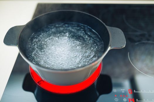 white boiling pot with hot steam on electrical induction cooktop