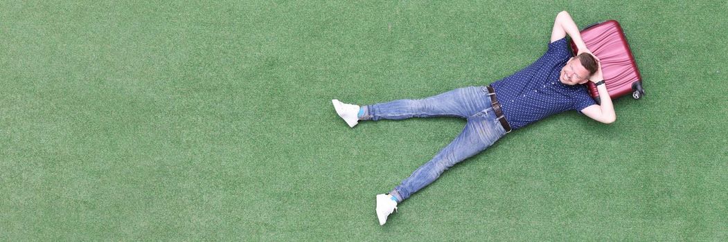 Young man lies on suitcase top view. Travel tourism and vacation concept