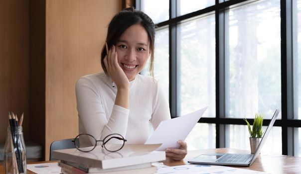 Portrait of smiling beautiful business asian woman with working in modern office desk using laptop computer, Business people employee freelance online marketing e-commerce telemarketing concept..