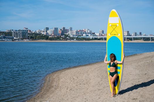 Caucasian woman walks along the beach and carries a sup board on the river in the city. Summer sport