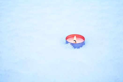 One lighting candle on snow surface with free space