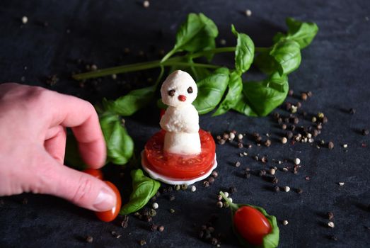 creative snowman canapes of mozzarella and tomatoes on a background of red poinsettia and a scattering of black pepper and green basil. High quality photo