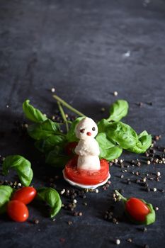 creative snowman canapes of mozzarella and tomatoes on a background of red poinsettia and a scattering of black pepper and green basil. High quality photo