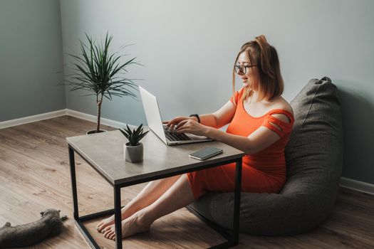 Caucasian Young Woman in Red Dress Working by Laptop from Home, Female Freelancer at Work, Remote Job