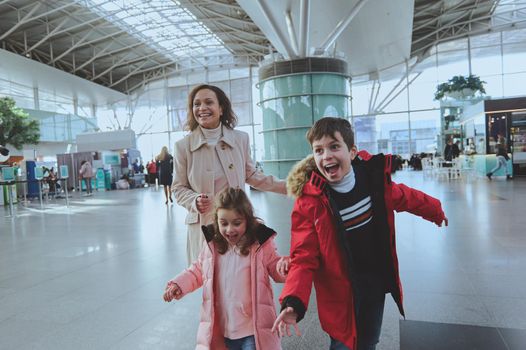 Happy multiethnic woman with her children running in airport arrivals terminal waiting room. Long-awaited family reuniting concept