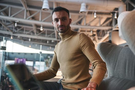 Portrait of a handsome multi-ethnic young man, passenger in casual pullover relaxing in the VIP lounge of the departure terminal of International airport