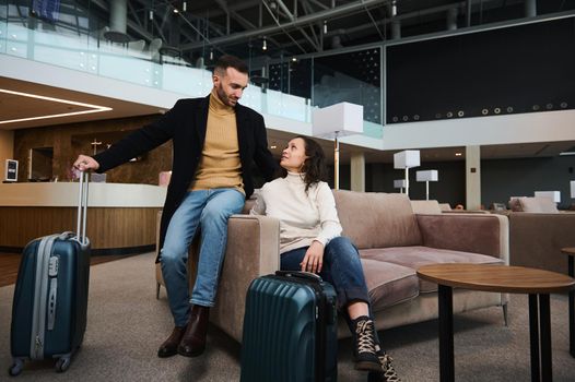 Charming young couple in love, married heterosexual couple, business partners, travelers, passengers with suitcase relaxing in the VIP lounge, waiting for flight check-in at international airport