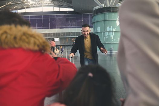 Happy young Middle Eastern man, father runs to meet his family after business trip at the international airport building. Long-awaited meeting at the airport arrivals terminal. Family reunion concept