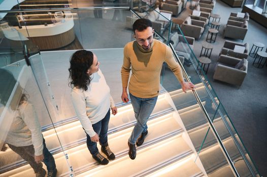 Handsome young man, guy and beautiful woman, partners, young couple, passengers communicating, standing on the second stage on the stairs in the VIP lounge of the international airport departure area