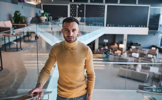 Handsome confident young man of Middle-Eastern ethnicity looks confidently at camera while walking up stairs in VIP lounge in international airport departure terminal, awaiting the flight boarding