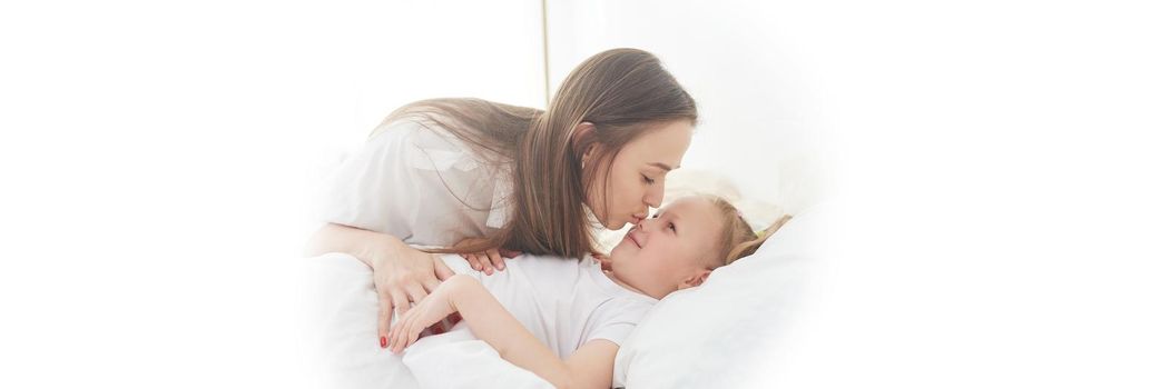 Awakening to a happy day. Mom wakes up her little daughter with a kiss on the bed in the bedroom. Web banner.