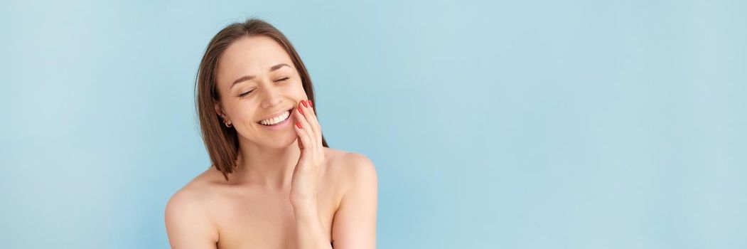 Smiling woman touching her face against a blue background. Natural beauty concept, happy woman. Web banner