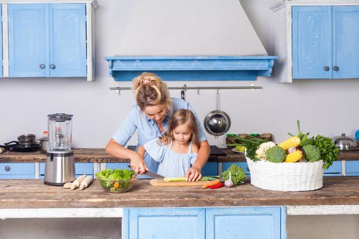 Young mother and lovely child cooking healthy breakfast together, cutting chopping vegetables, preparing vegetarian salad in modern kitchen, fresh green vegetables on table, vegan food, diet nutrition