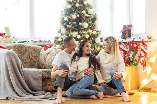 Christmas Family. Happiness. Portrait of dad, mom and daughter sitting at home near the Christmas tree.