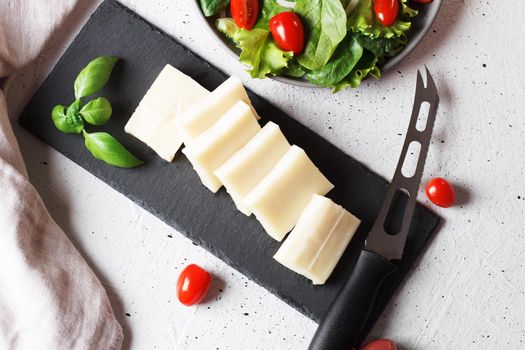 A piece of fresh sliced halloumi on a slate board with cherry tomatoes and spinach leaves. Preparing to cook cheese on the grill. Top view