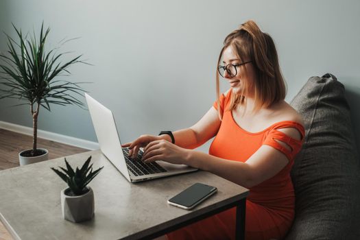 Caucasian Young Woman in Red Dress Working by Laptop from Home, Female Freelancer at Work, Remote Job